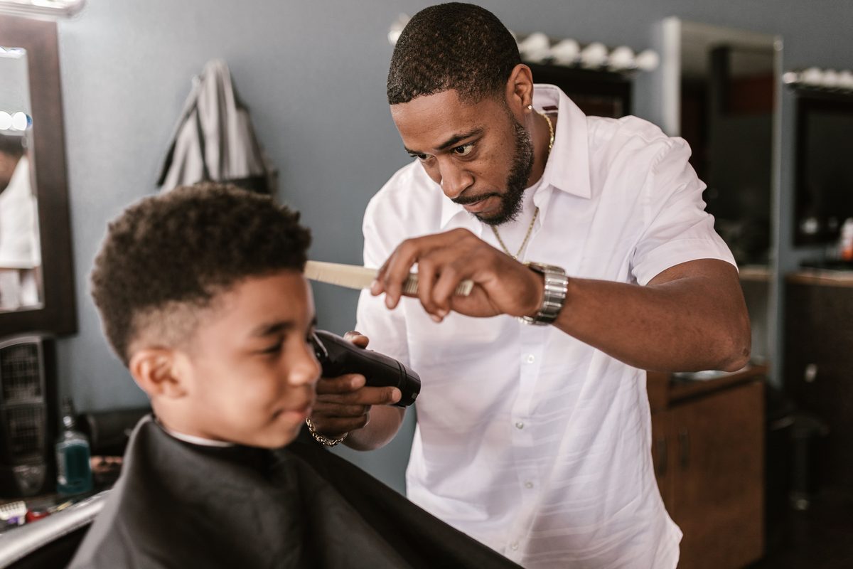 Barber carefully trimming a school-age boy’s textured hair