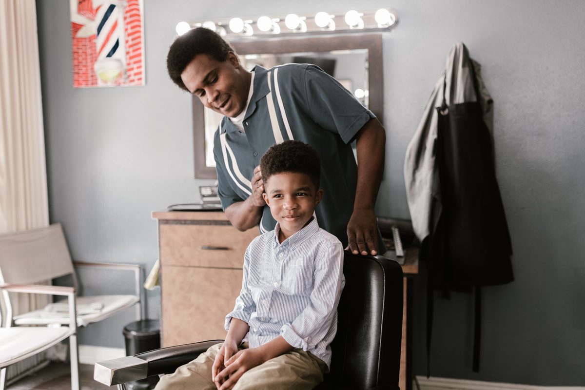 A smiling boy receives a haircut from a barber in a stylish barbershop setting.