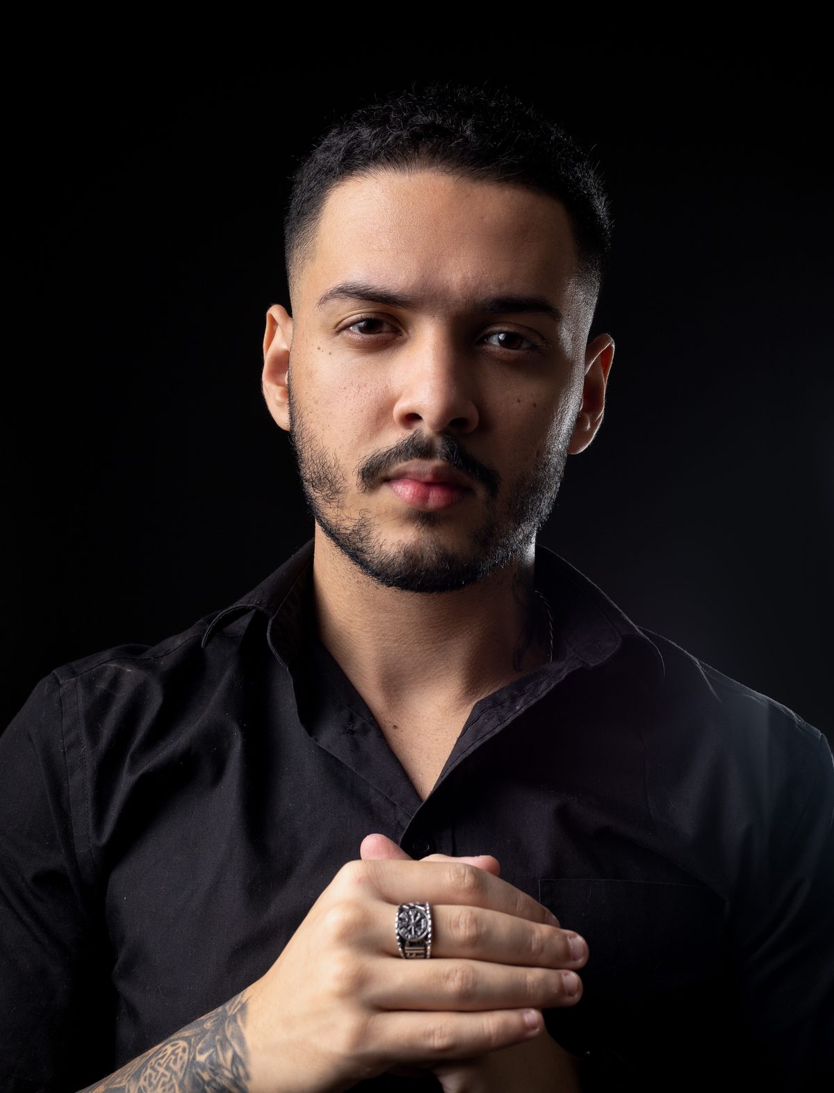 Confident black shirt beard hairstyle shown on a young man.