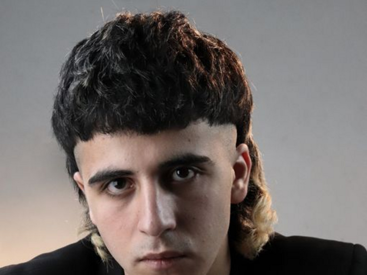 Studio portrait showing a modern mullet with a short textured front, exposed ear and visibly longer back
