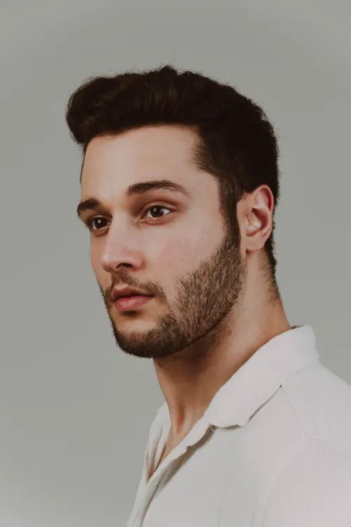 Professional man in profile with a controlled short haircut and neat stubble.
