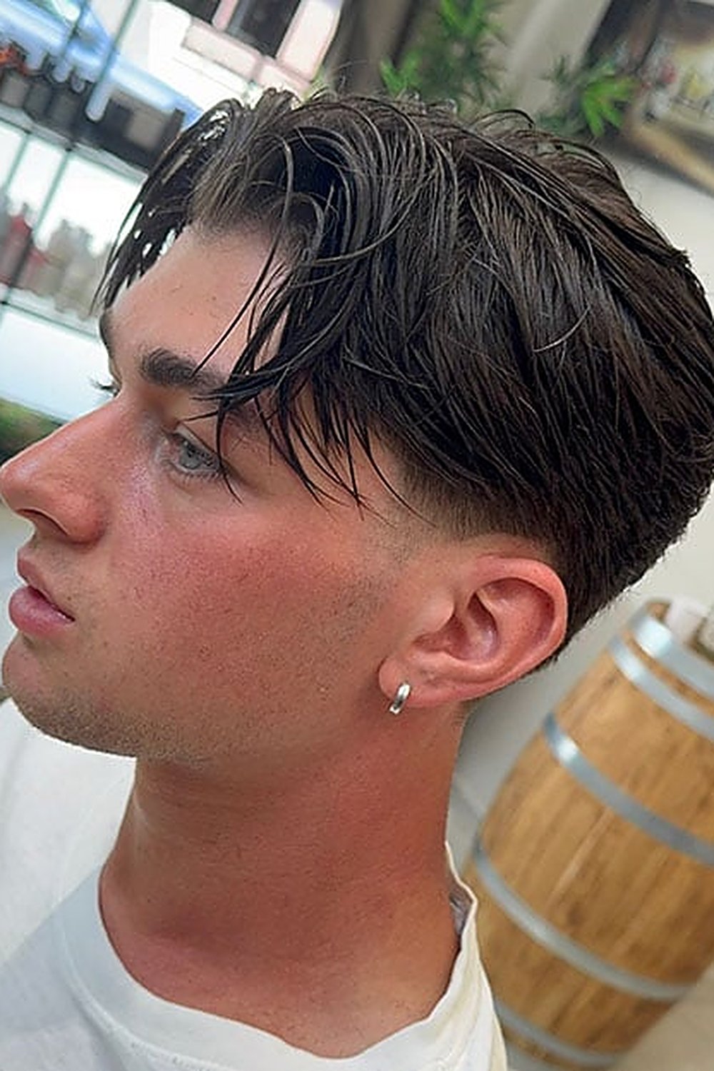 Young man with a wet-look middle part taper fade — slicked dark curtains with faded sides in a barbershop