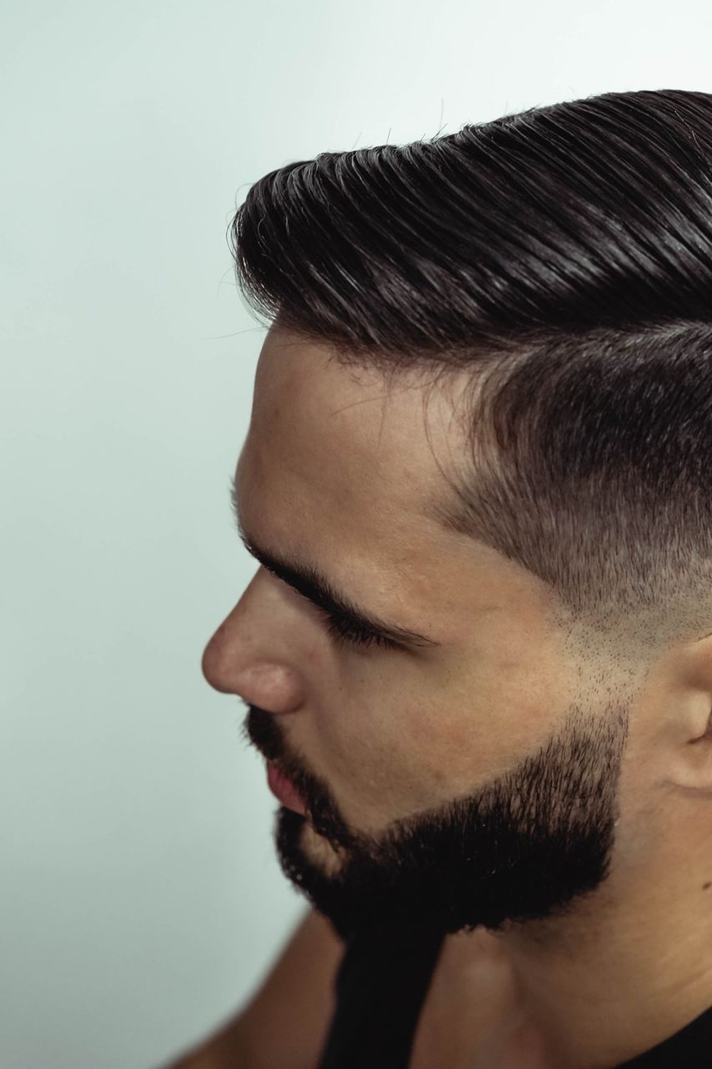 Side profile of a bearded man with a neat side-part low fade haircut