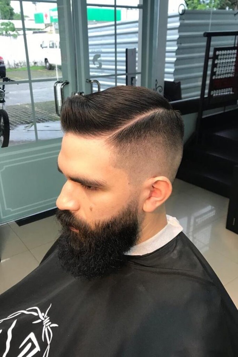 Man in a barber chair with an Ivy League haircut — hard side part and taper fade
