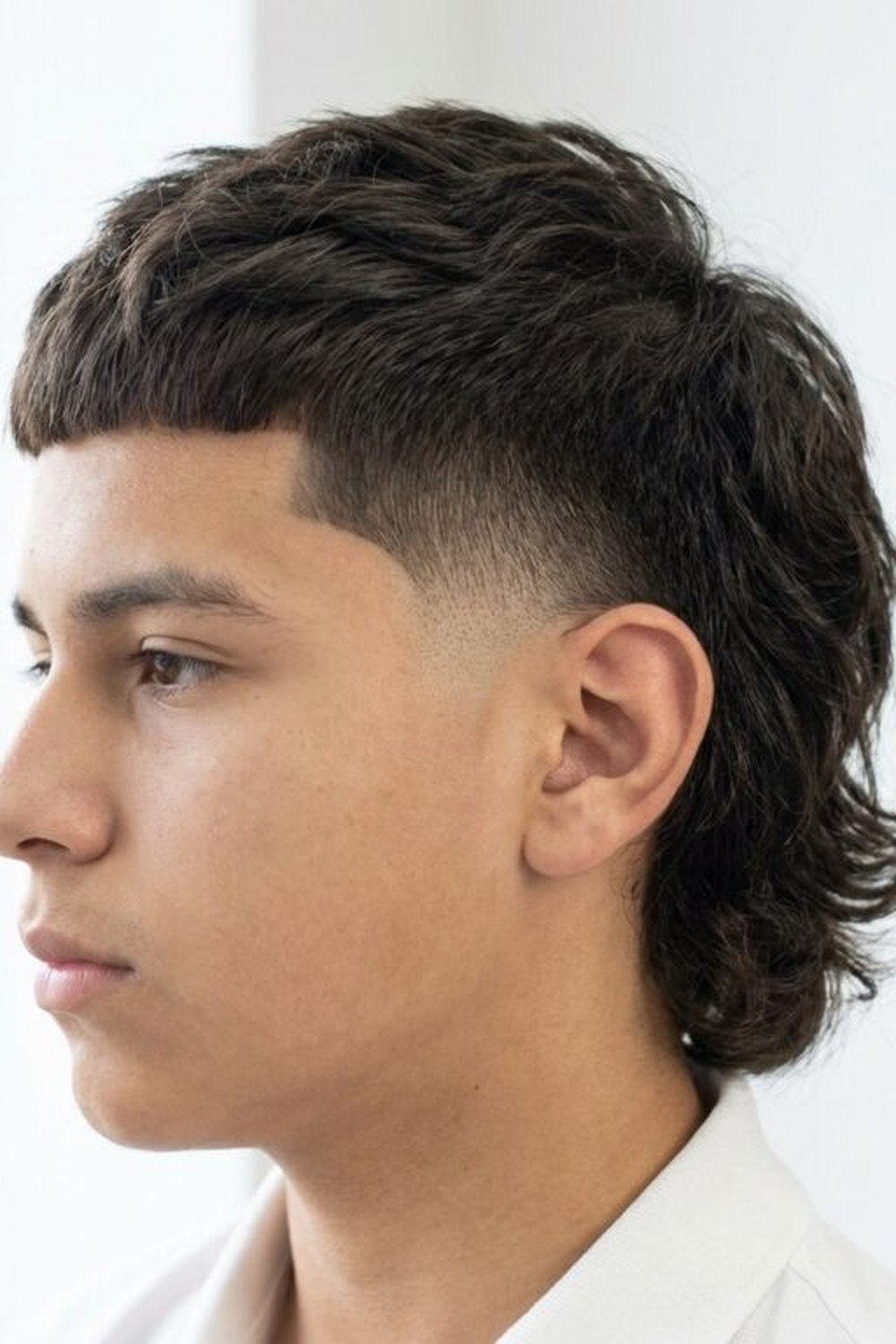 Teenager with a burst fade mullet — short fringe front, faded sides, length at the back