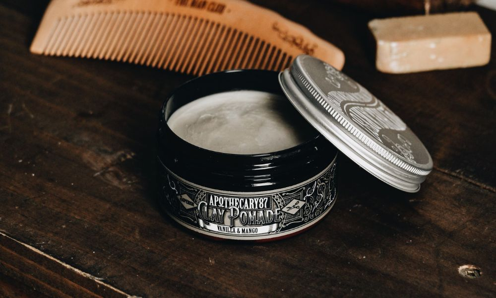 Open pomade tin beside a wooden comb