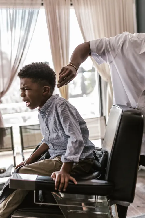 Boy seated in a barber chair before a haircut