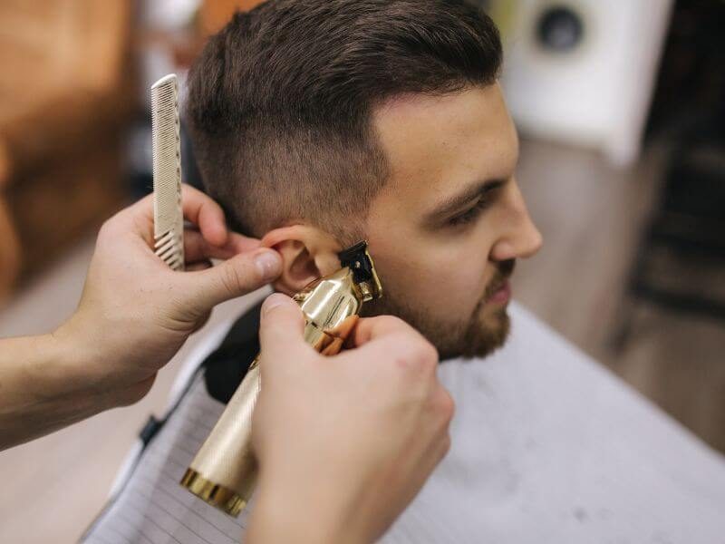 Barber refining the taper around the ear with clippers and comb.